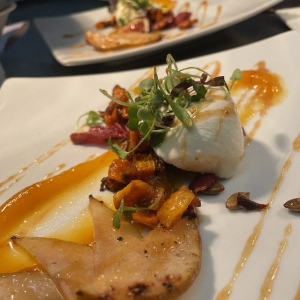 Lattitude Restaurant's appetizer with burrata, roasted squash, pears, and microgreens on a white plate.