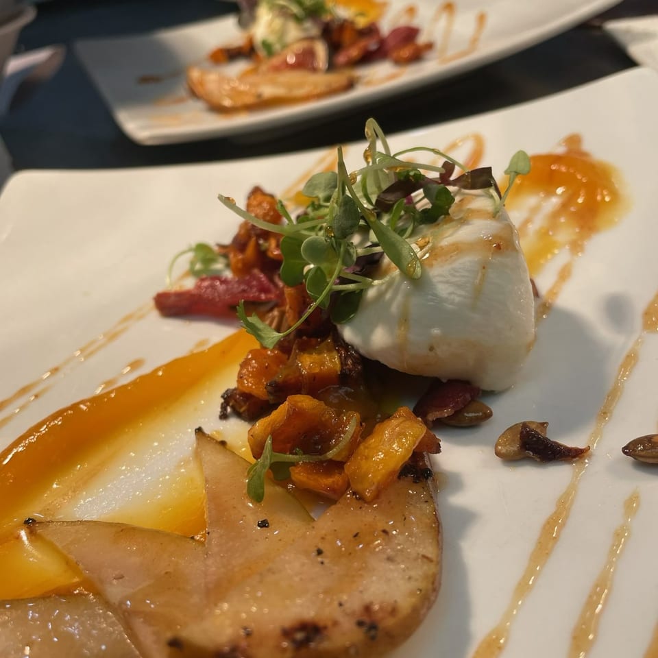 Lattitude Restaurant's appetizer with burrata, roasted squash, pears, and microgreens on a white plate.