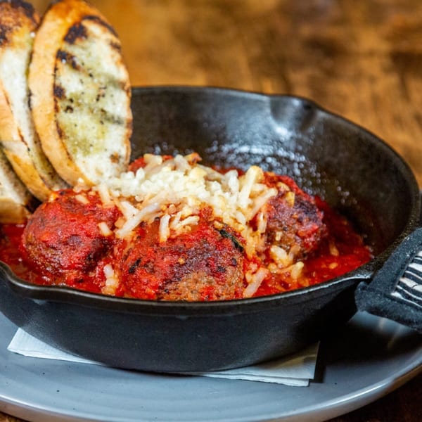 Meatballs in red sauce topped with cheese, served in a cast iron skillet with grilled bread.