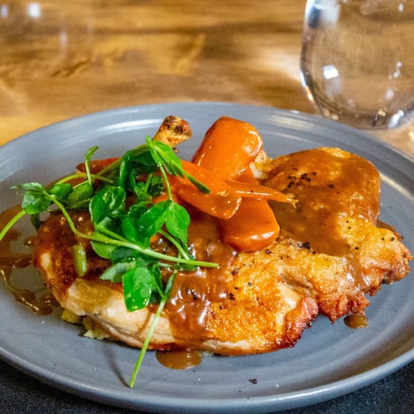 Crispy-skinned chicken with gravy, carrots, and fresh greens on a gray plate at Lattitude Restaurant.