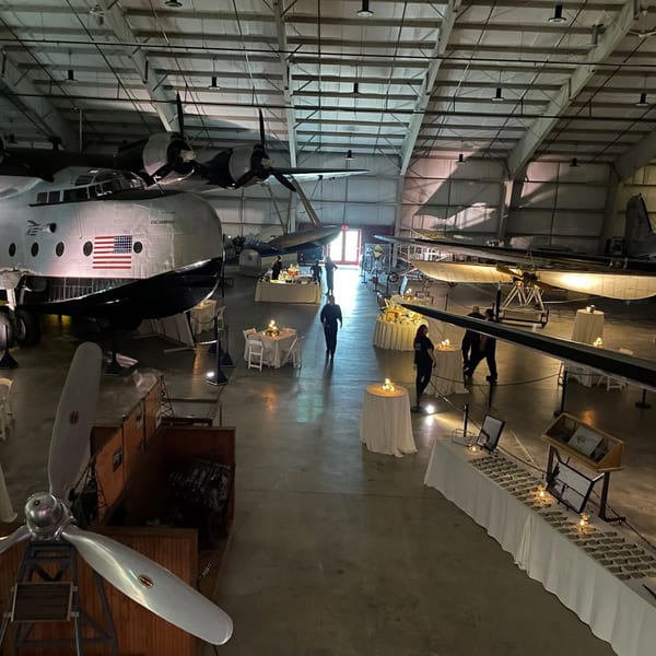 A large event space with vintage airplanes, white-draped tables, and people mingling.