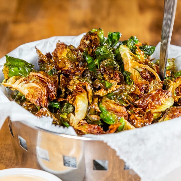 Crispy fried Brussels sprouts with a fork in a metal basket lined with white paper.