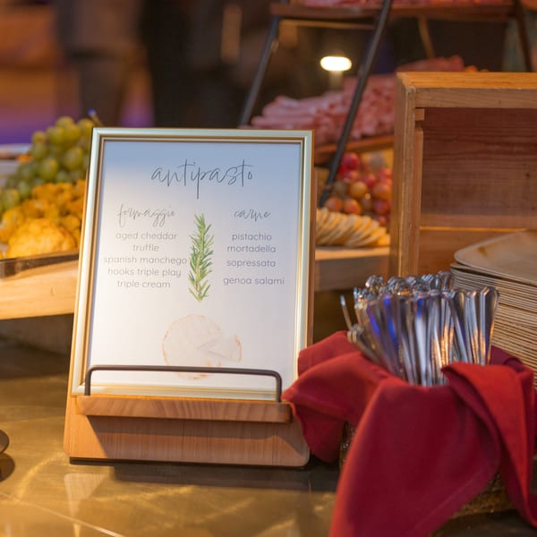 An antipasto sign lists cheeses and meats, with cutlery and food platters in the background.