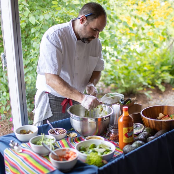 A chef in a white coat prepares guacamole at an outdoor Lattitude Restaurant food station.